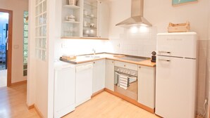 Una cocina funcional con armarios blancos, horno empotrado, pileta de acero inoxidable y refrigerador compacto.