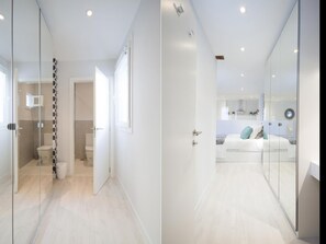 Une chambre moderne avec une cloison en verre, un lit blanc et une salle de bain ouverte avec des toilettes et une douche.