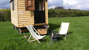A small wooden cabin with a door open, a grill, two lawn chairs, and a basket on a grassy field. - Marshwood Farm B&B (Salisbury)
