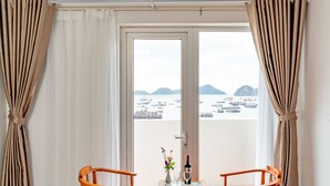 A room with a table and two chairs, a bottle of wine, and a vase with flowers. - Draco QK3 Cat Ba (Hai Phong)