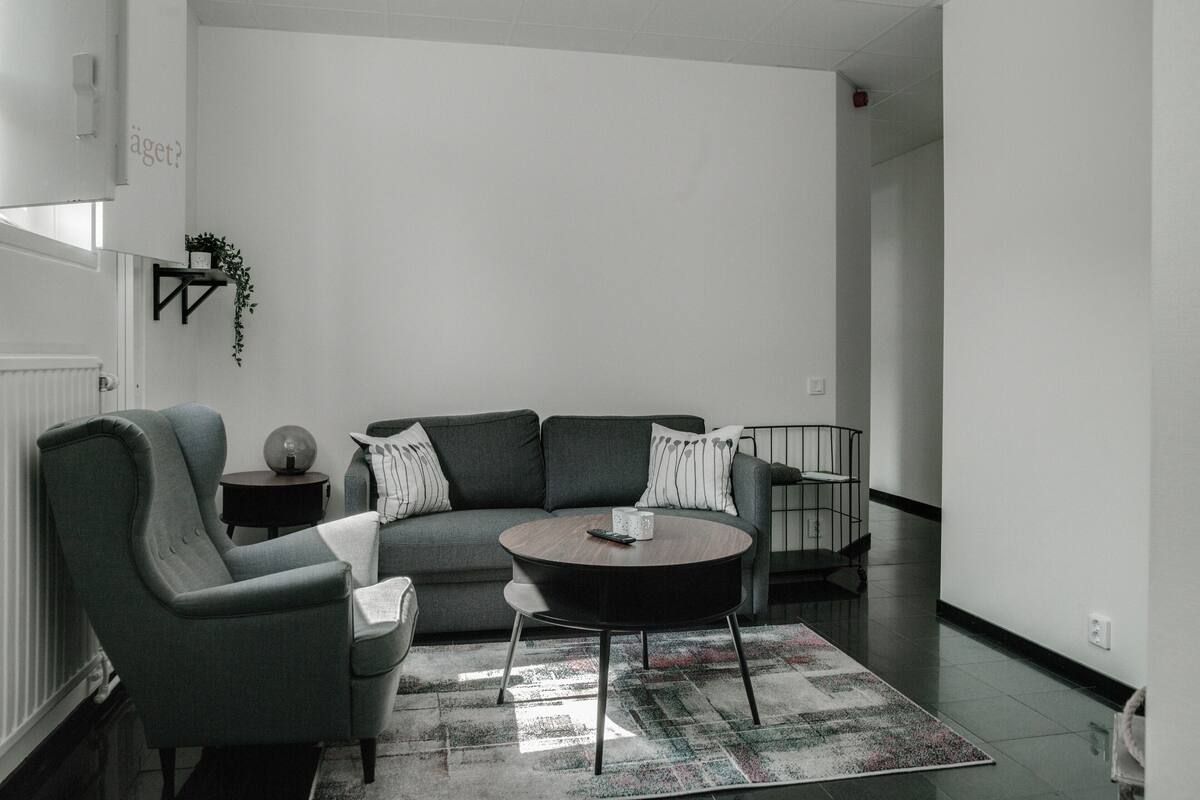 A modern living room with a grey sofa, armchairs, a coffee table, and a patterned rug.