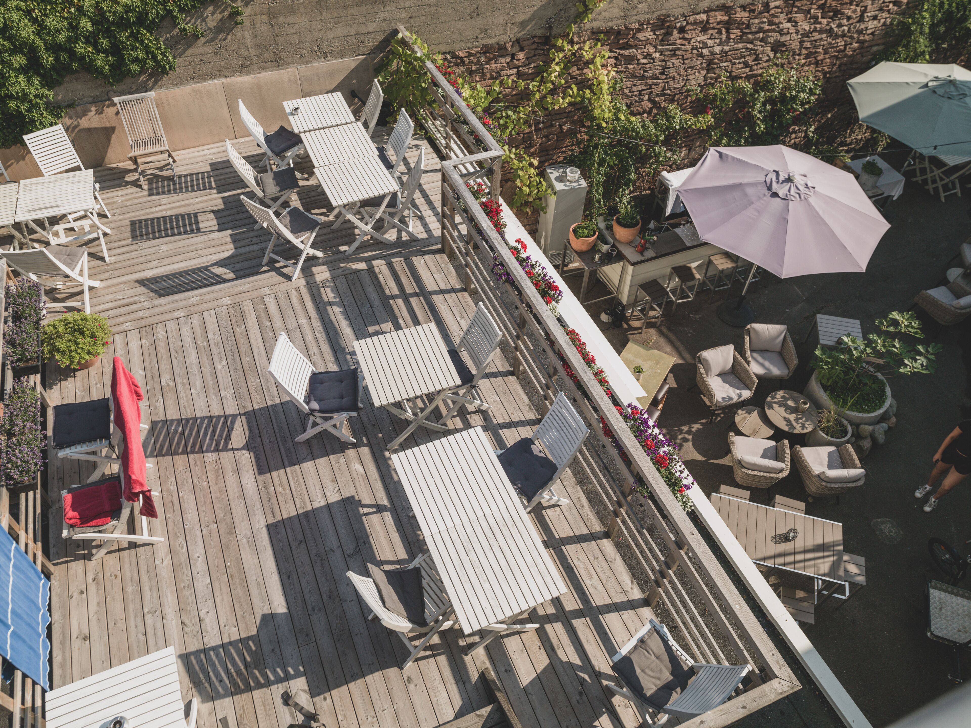 An outdoor deck with multiple seating areas, including lounge chairs and tables, surrounded by potted plants and umbrellas.