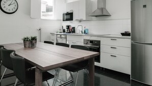 A modern kitchen with white cabinets, a stainless steel refrigerator, a microwave, and a clock on the wall.