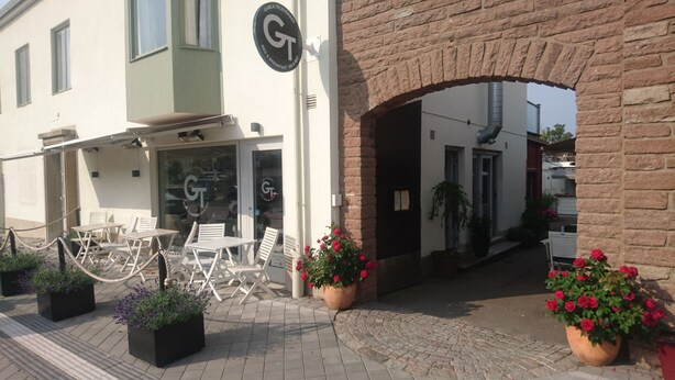 A restaurant with outdoor seating, a brick archway entrance, and potted plants.