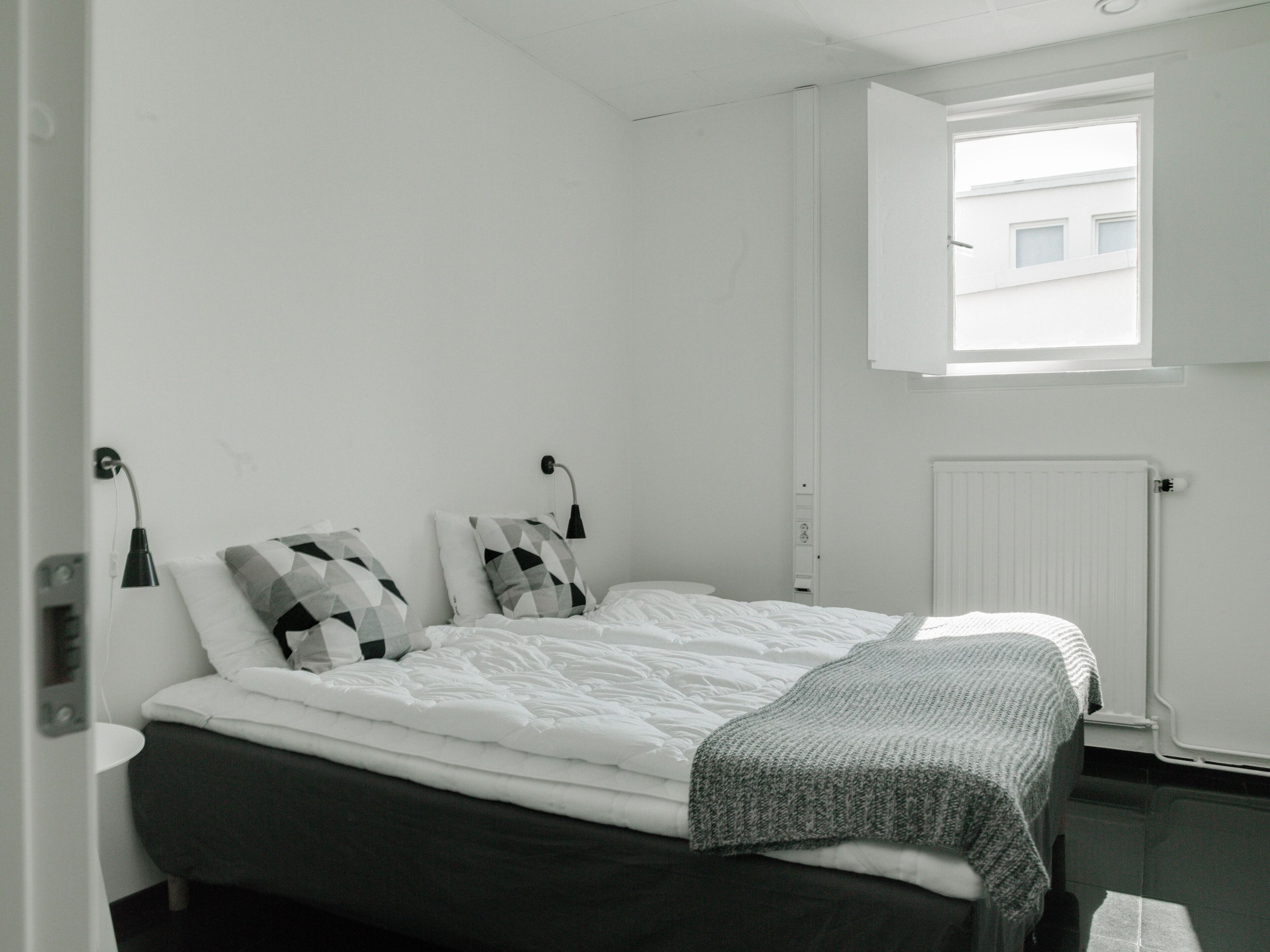 A bedroom with a bed, two bedside tables, a window, and a radiator.