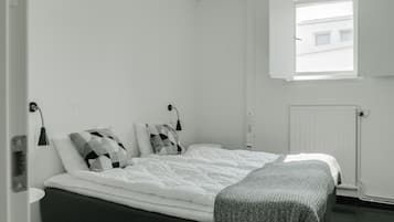 A bedroom with a bed, two bedside tables, a window, and a radiator.