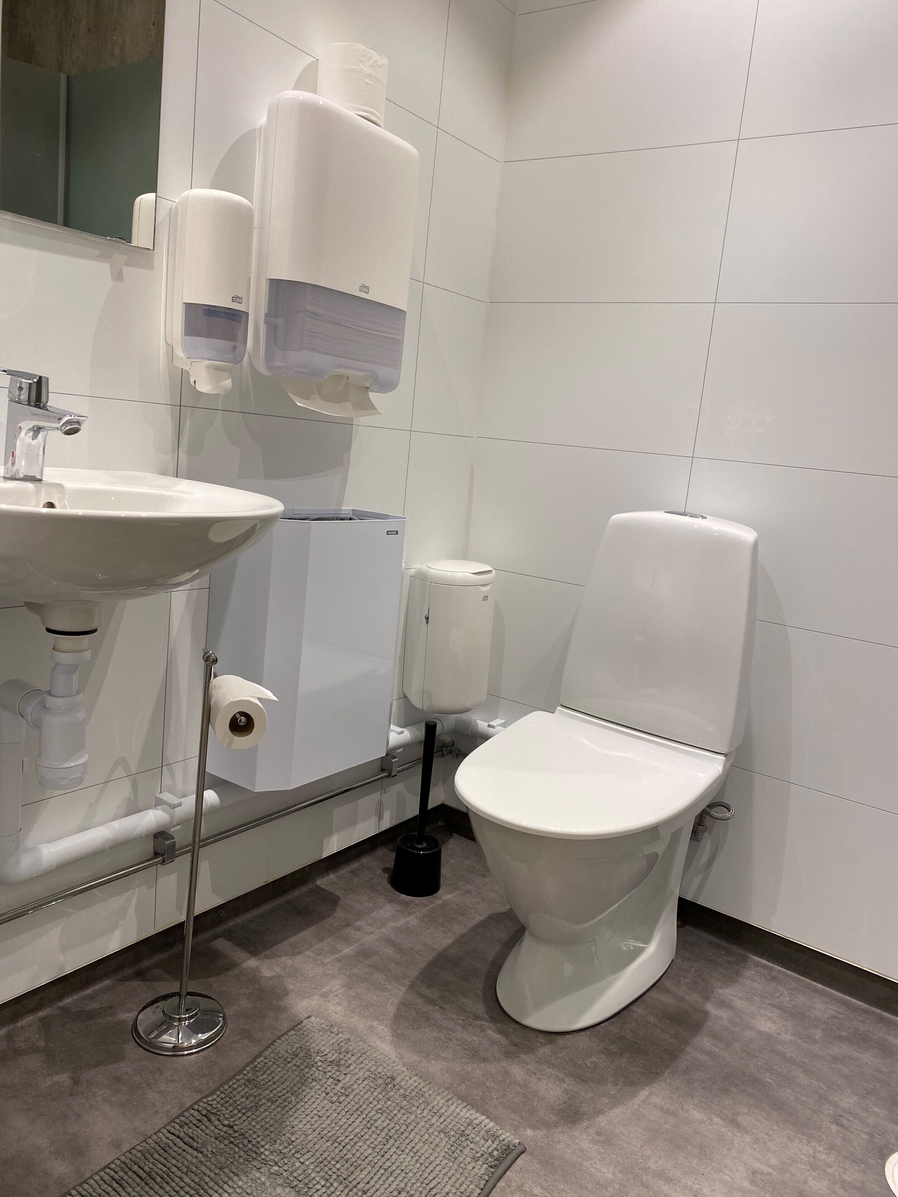 Et moderne badeværelse med hvid vask, toilet og håndtørrer.