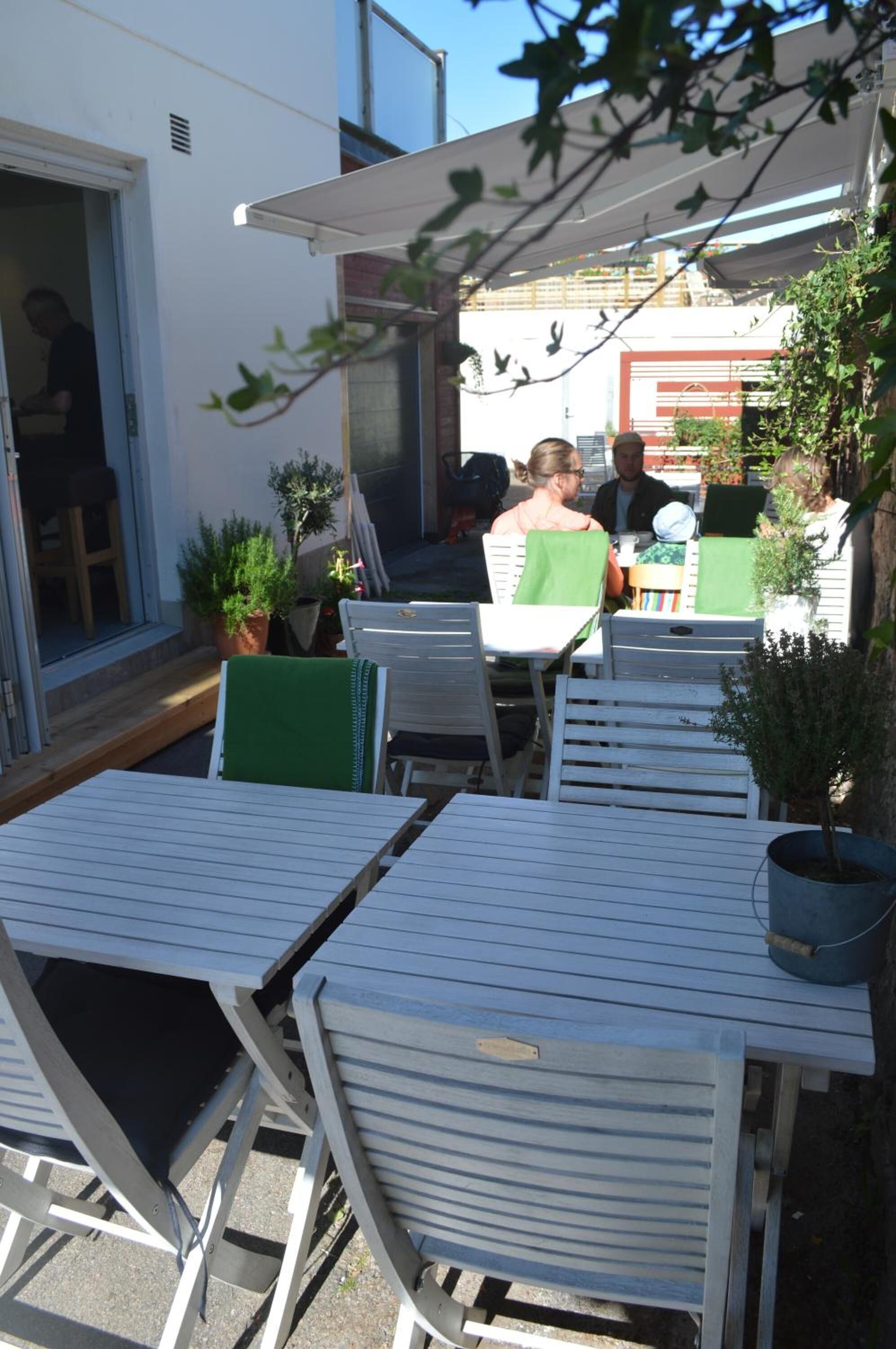 An outdoor seating area with white tables and chairs, potted plants, and a covered patio.