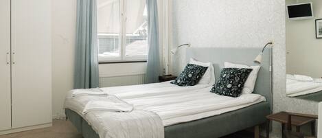 A neatly arranged bedroom with a bed, bedside lamps, a window with curtains, a bedside table, and a mirror on the wall.
