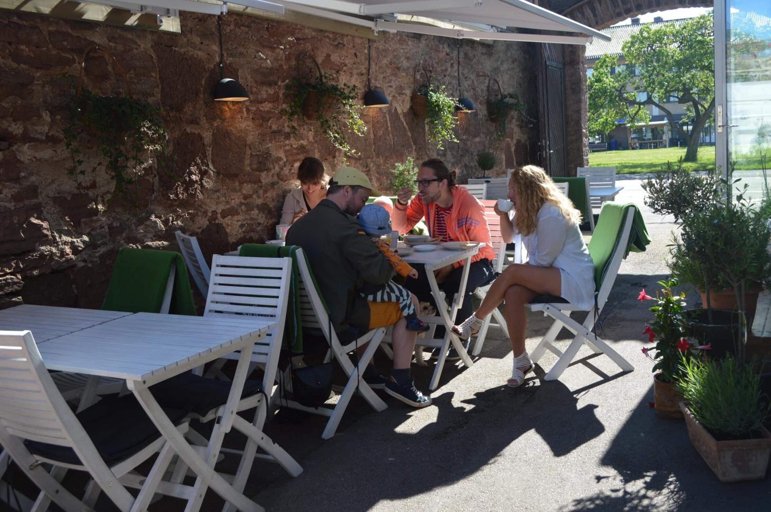An outdoor seating area with white metal tables and chairs, a stone wall, and hanging plants.