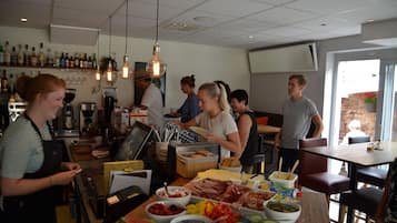 Un restaurante con zona de bar, un bufé con diferentes opciones de comida y una sala de estar con mesas y sillas.
