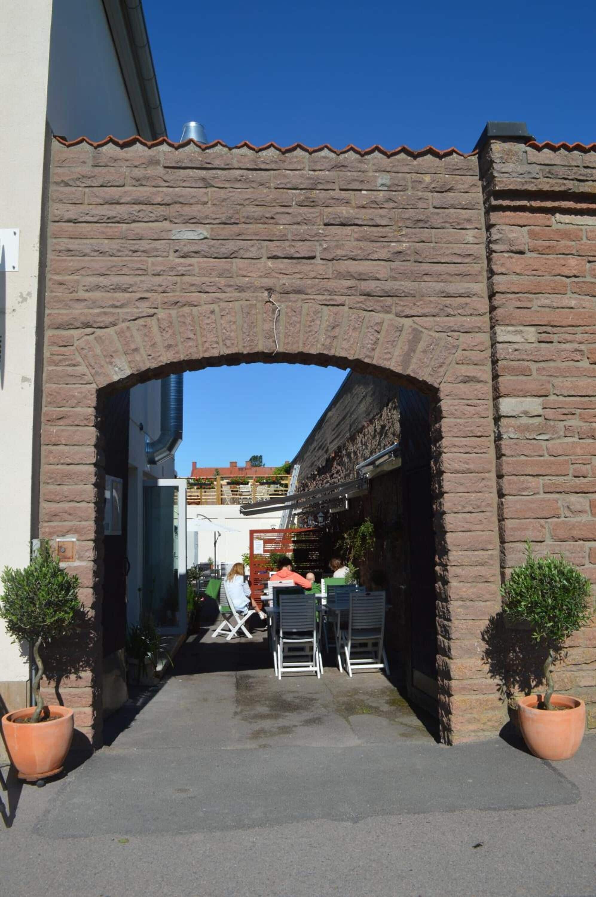 En buet murindgang til en bygning med terrasse og krukker med planter.