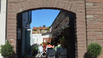 En buet murindgang til en bygning med terrasse og krukker med planter.