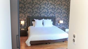 A hotel room with a large bed, wooden flooring, and patterned wallpaper.