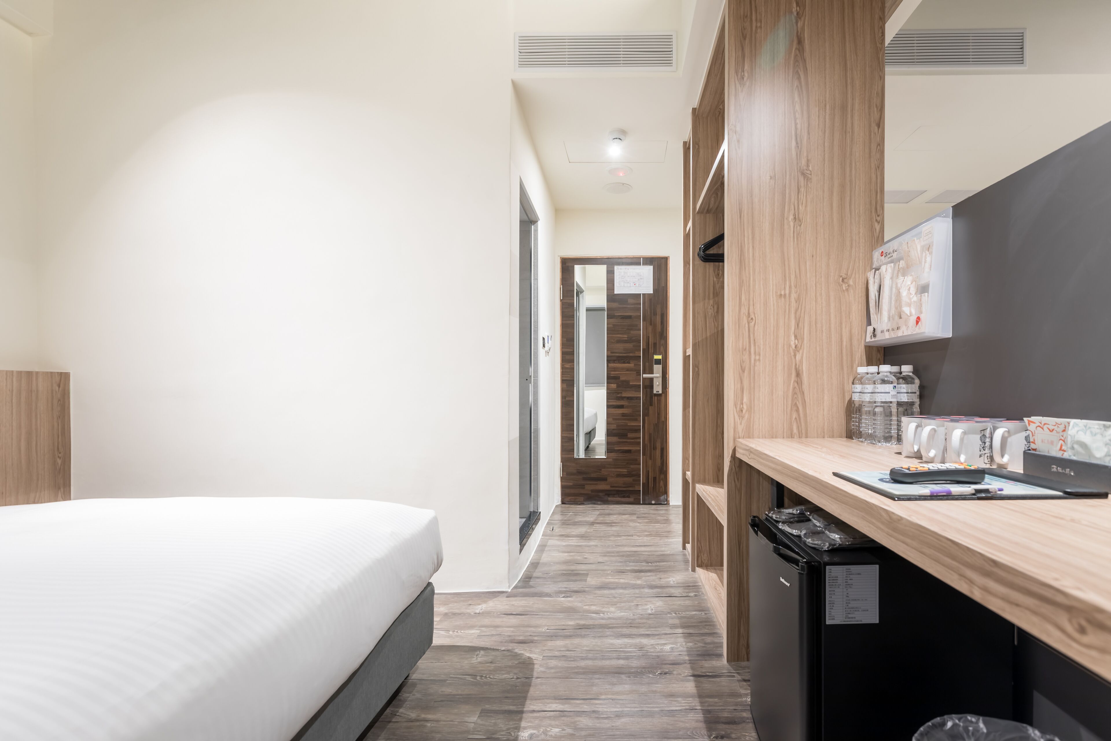 Habitación de hotel con cama, escritorio con computadora, cesto de basura y refrigerador pequeño.