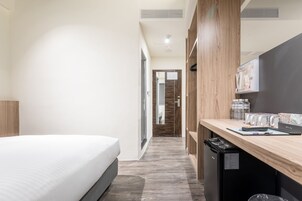 Habitación de hotel con cama, escritorio con computadora, cesto de basura y refrigerador pequeño.