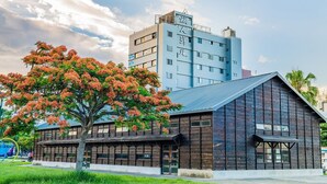 A modern building with a large tree in front, a blue building in the background, and a clear sky. - Traveller Inn Rail Haus (Taitung)