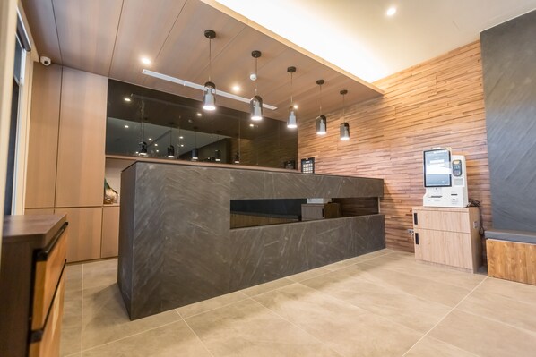 A modern reception area with a marble counter, wooden paneling, and a self-service kiosk.