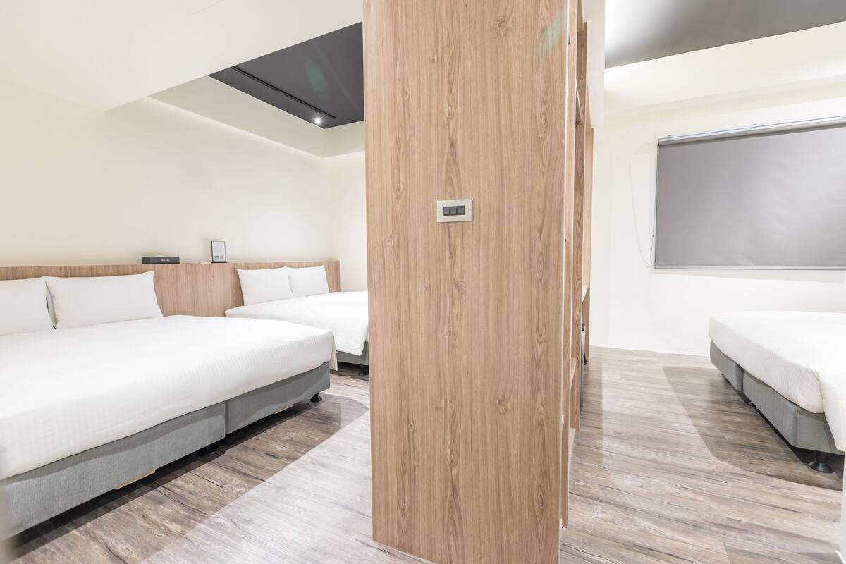 A modern hotel room with two single beds, a wooden accent wall, a large window, and a flat-screen TV.