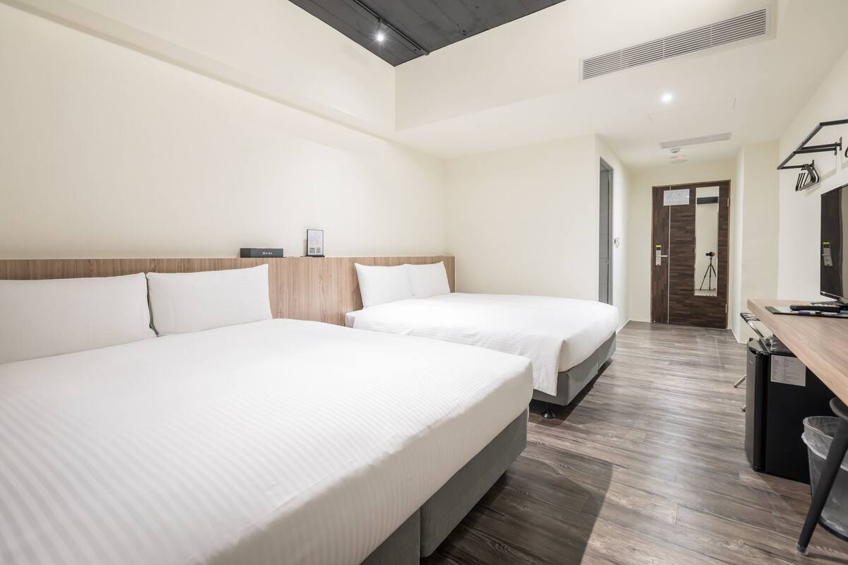 A hotel room with two beds, a desk, and a mirror.