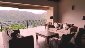 A spacious living area with a sofa, chairs, and a coffee table. A large window offers a view of a mountainous landscape. - Levita (Maberiyatenna)