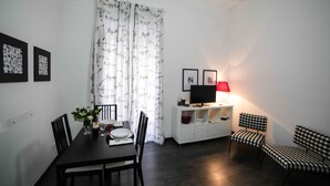 A dining area with a table set for two, a TV on a white cabinet, and a bench with checkered cushions. - Amazing Politeama house (Palermo)