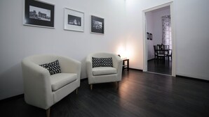 A modern living room with two white armchairs, a small side table, and three framed black-and-white photographs on the wall. - Amazing Politeama house (Palermo)