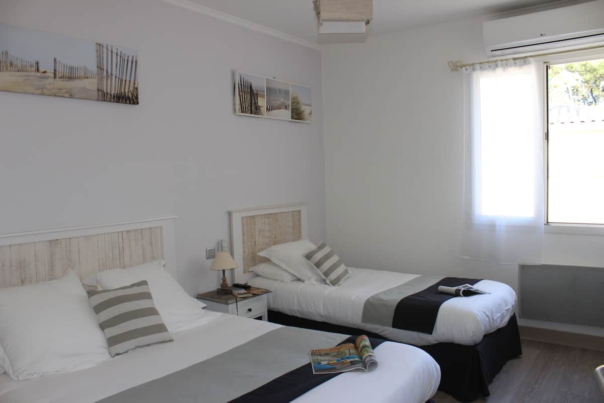 Een hotelkamer met twee bedden, een nachtkastje, een lamp en een raam met uitzicht op de omgeving.