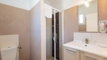 A bathroom with a glass-enclosed shower, a toilet, and a sink with a mirror above it.
