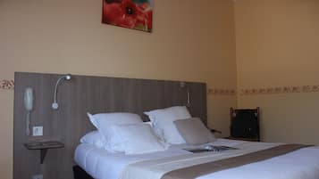 A hotel room with a large bed, a bedside telephone, a small table, and a wall-mounted lamp.
