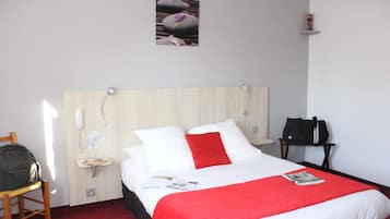 A hotel room with a bed, a chair, a desk, a telephone, and a wall-mounted shelf.