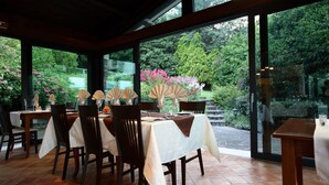 Comedor con mesas dispuestas para cuatro, ventanas amplias y vista a un jardín.
