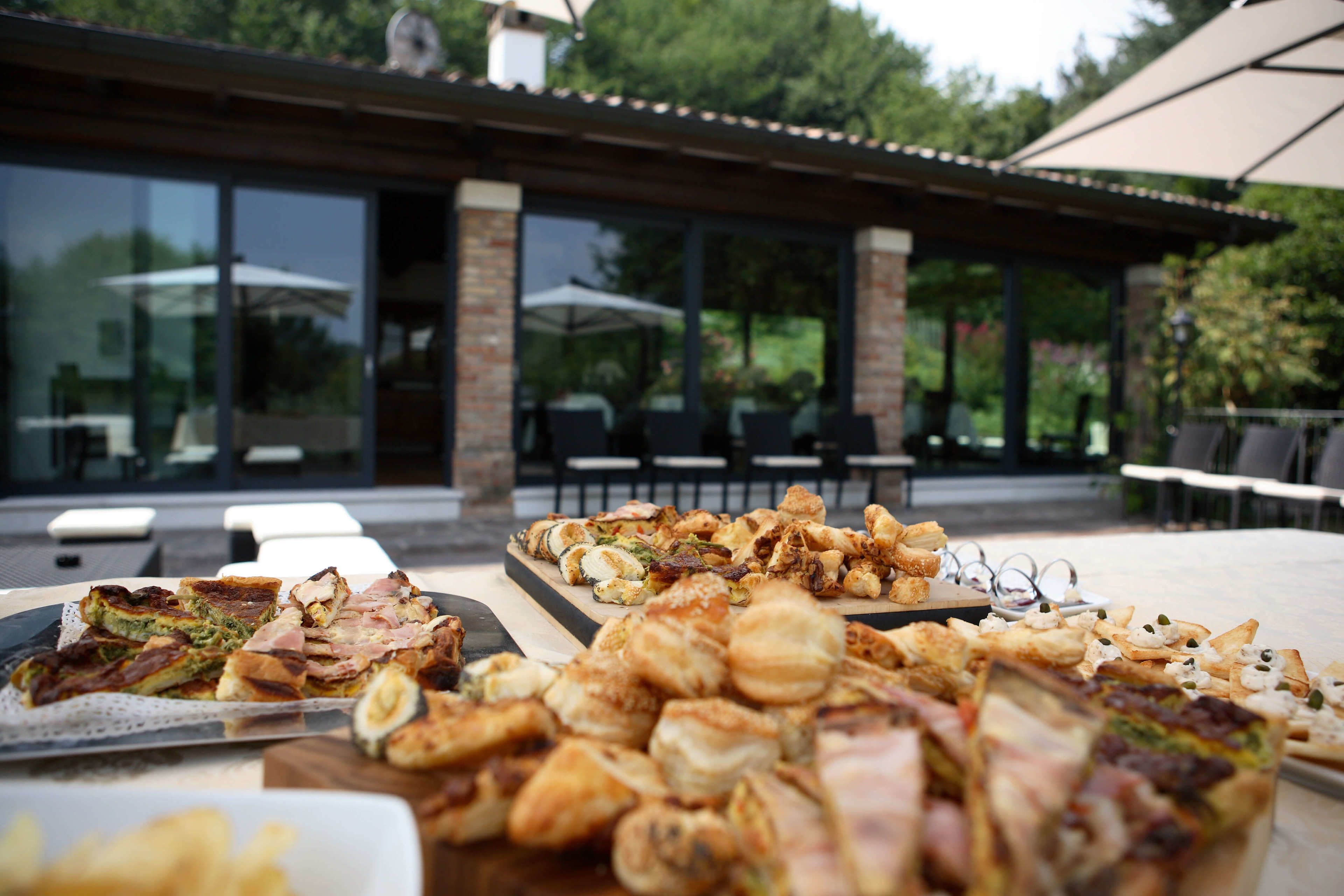Un área de comedor al aire libre con diferentes alimentos sobre una mesa, rodeada de asientos exteriores y un porche cubierto.