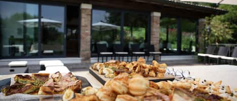 Un área de comedor al aire libre con diferentes alimentos sobre una mesa, rodeada de asientos exteriores y un porche cubierto.