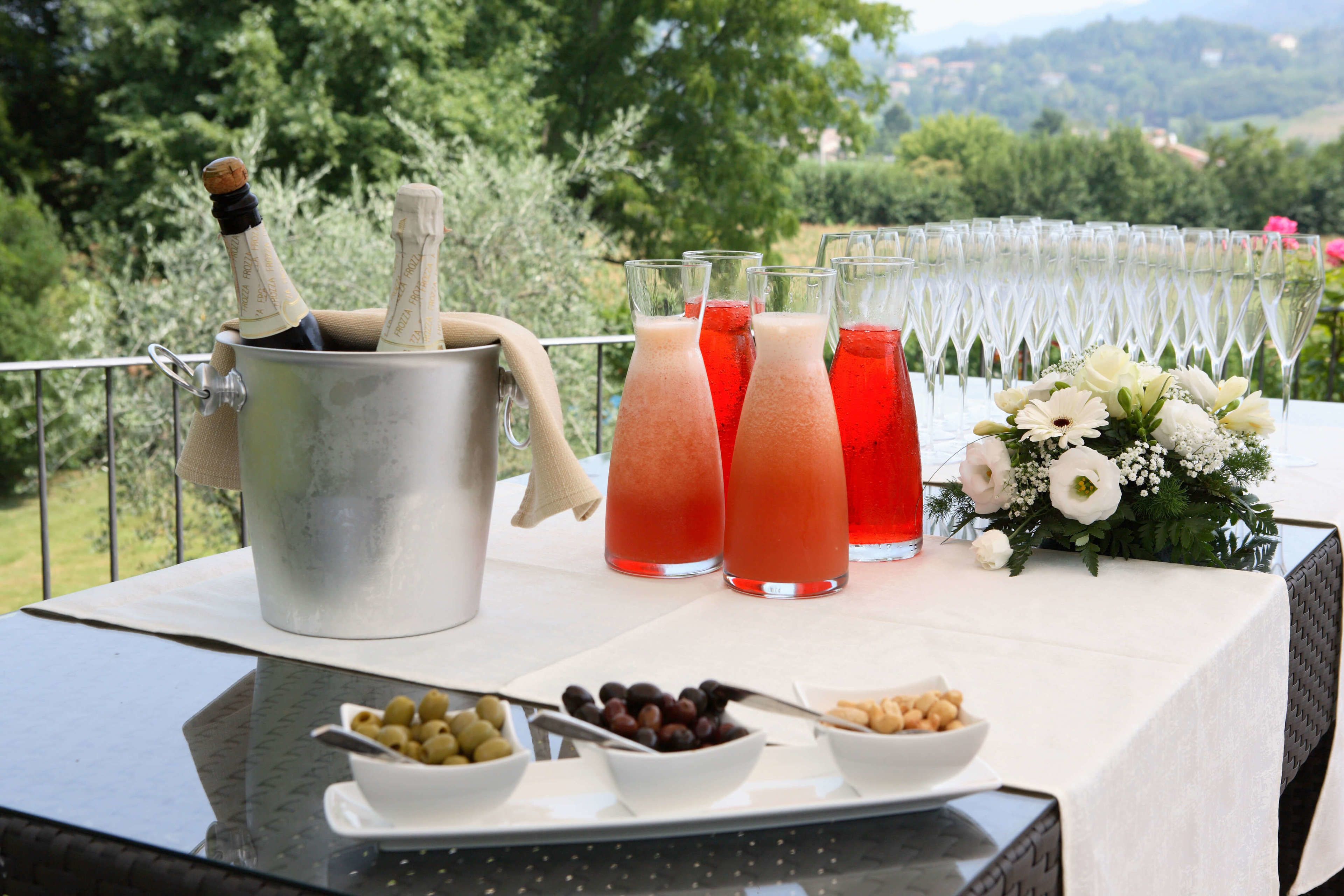 A table set with a bottle of champagne, three glasses of red drink, and a bouquet of flowers.