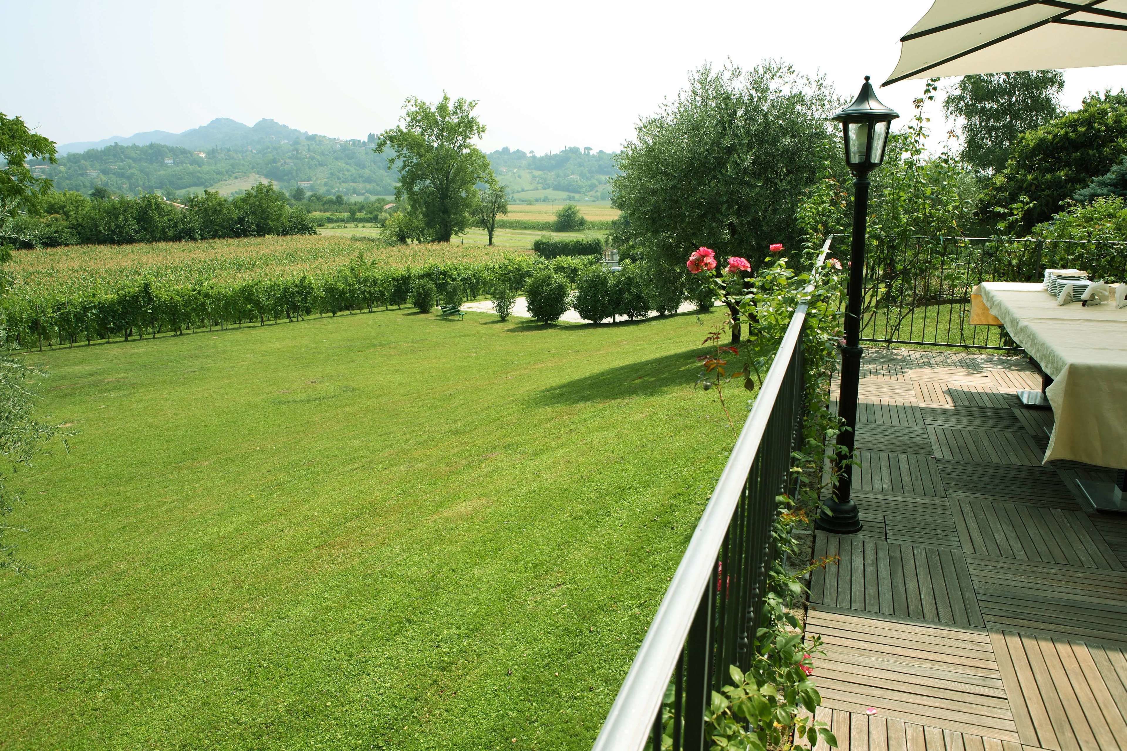 A balcony with a view of a well-maintained lawn and distant hills.