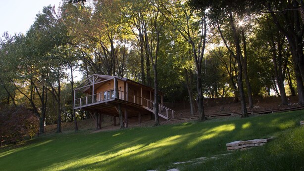 Una cabaña de madera con balcón, rodeada de árboles y un espacio cubierto de césped.