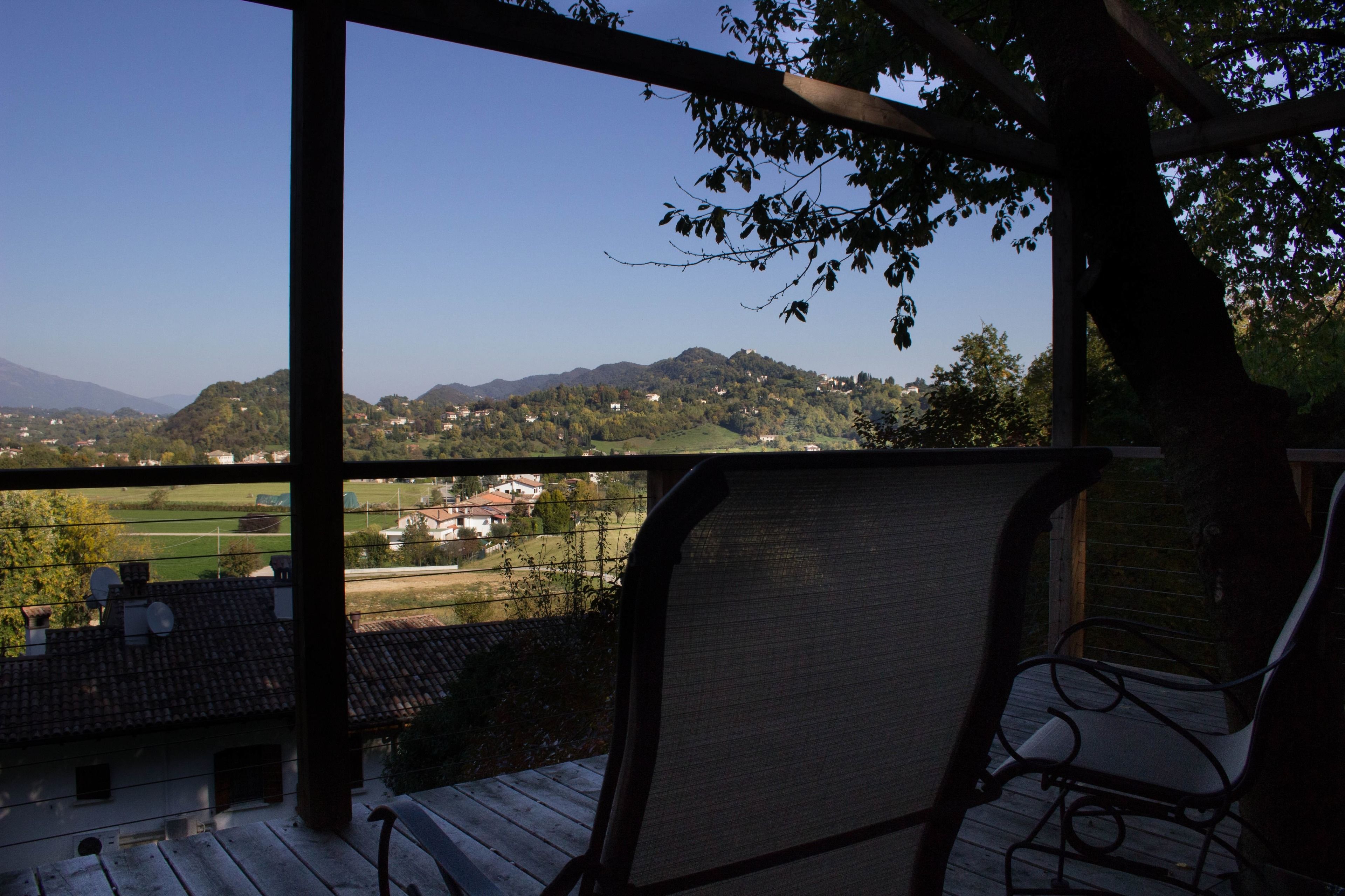 Ein überdachter Außenbereich mit Blick auf eine hügelige Landschaft und Gebäude in der Ferne.