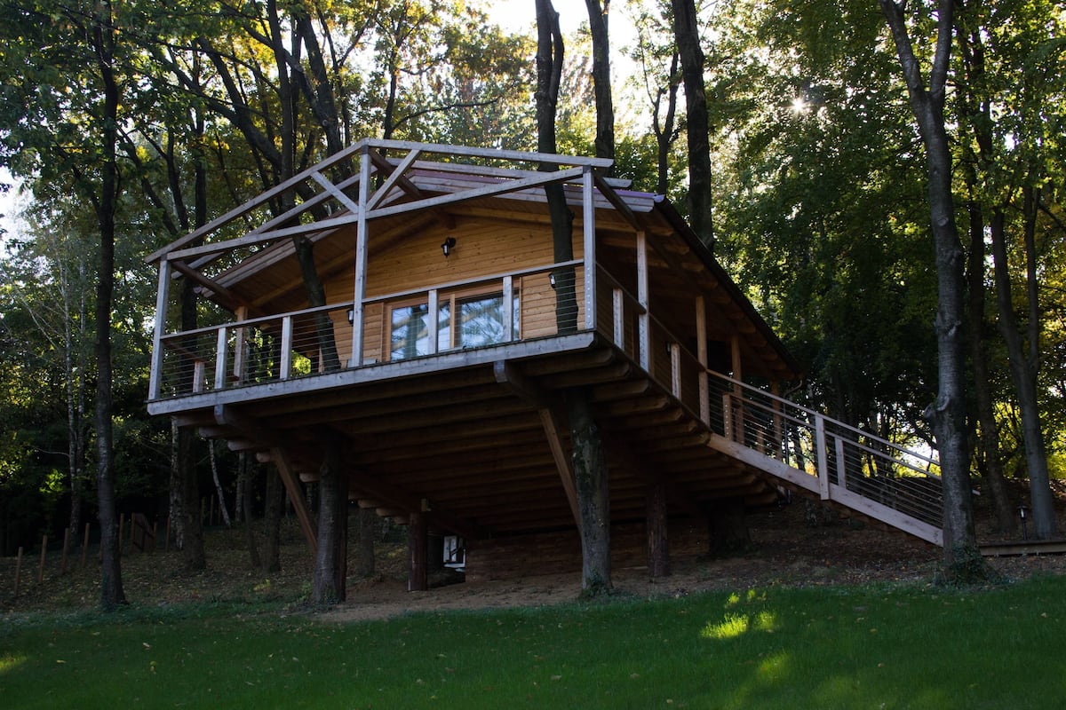A wooden treehouse with a balcony, surrounded by trees.