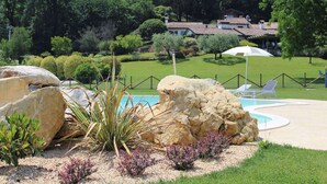 Zona ajardinada con piscina, rocas grandes y césped delimitado por una valla.
