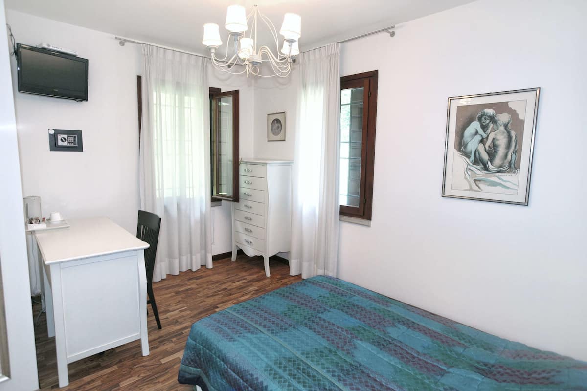 A bedroom with a bed, a desk, a chair, a dresser, a television, and a painting on the wall.