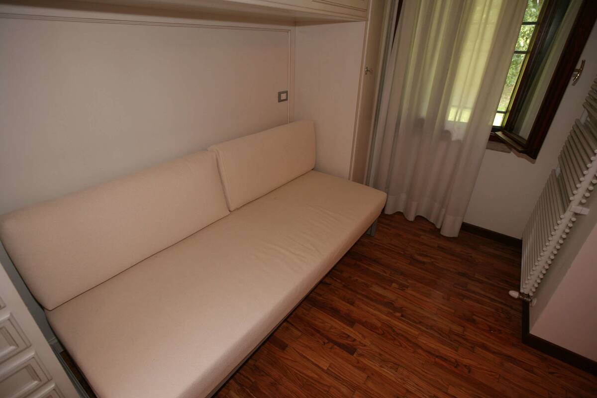 A room with a beige sofa, wooden flooring, a radiator, and a window with curtains.