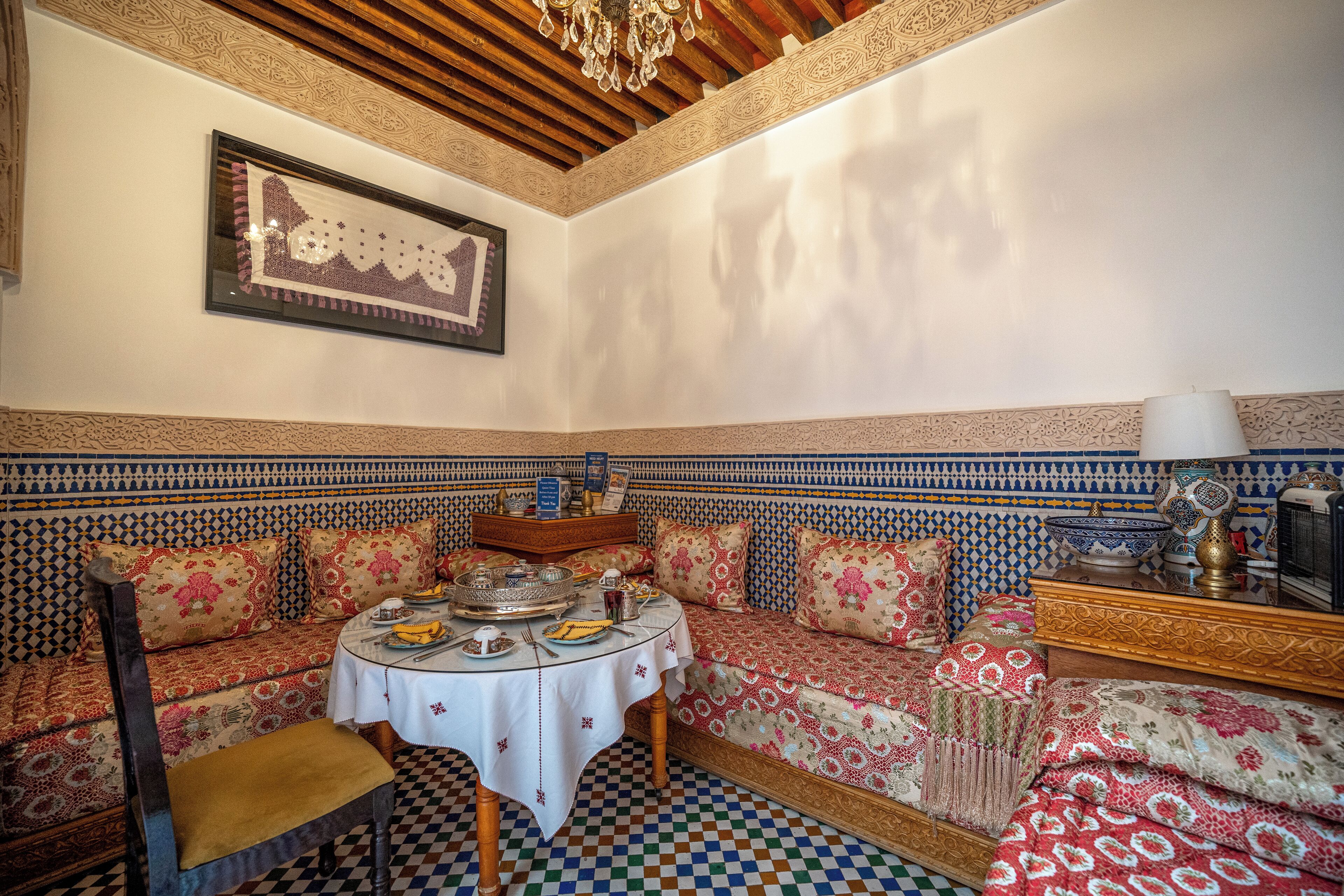 Un intérieur marocain traditionnel, avec un canapé à motifs, une table ronde recouverte d’une nappe blanche et un plafond décoratif.