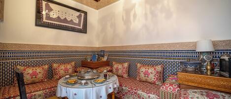 Un interior tradicional marroquí con un sofá estampado, una mesa redonda con mantel blanco y un techo decorativo.