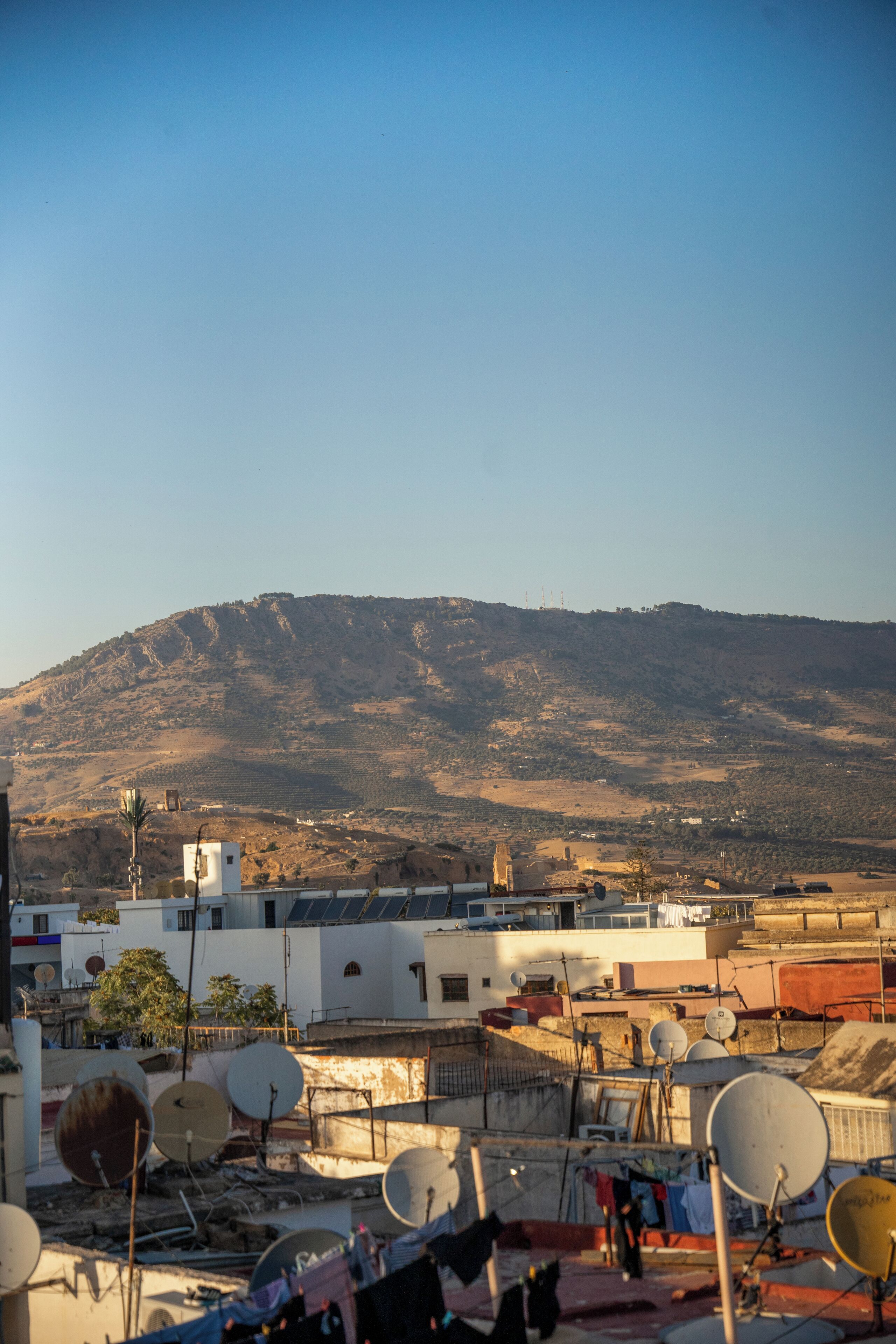 A residential area with satellite dishes, a hillside in the background, and a clear sky.