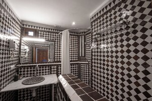 Uma casa de banho com padrão de azulejos xadrez, uma pia com espelho redondo e zona de duche.