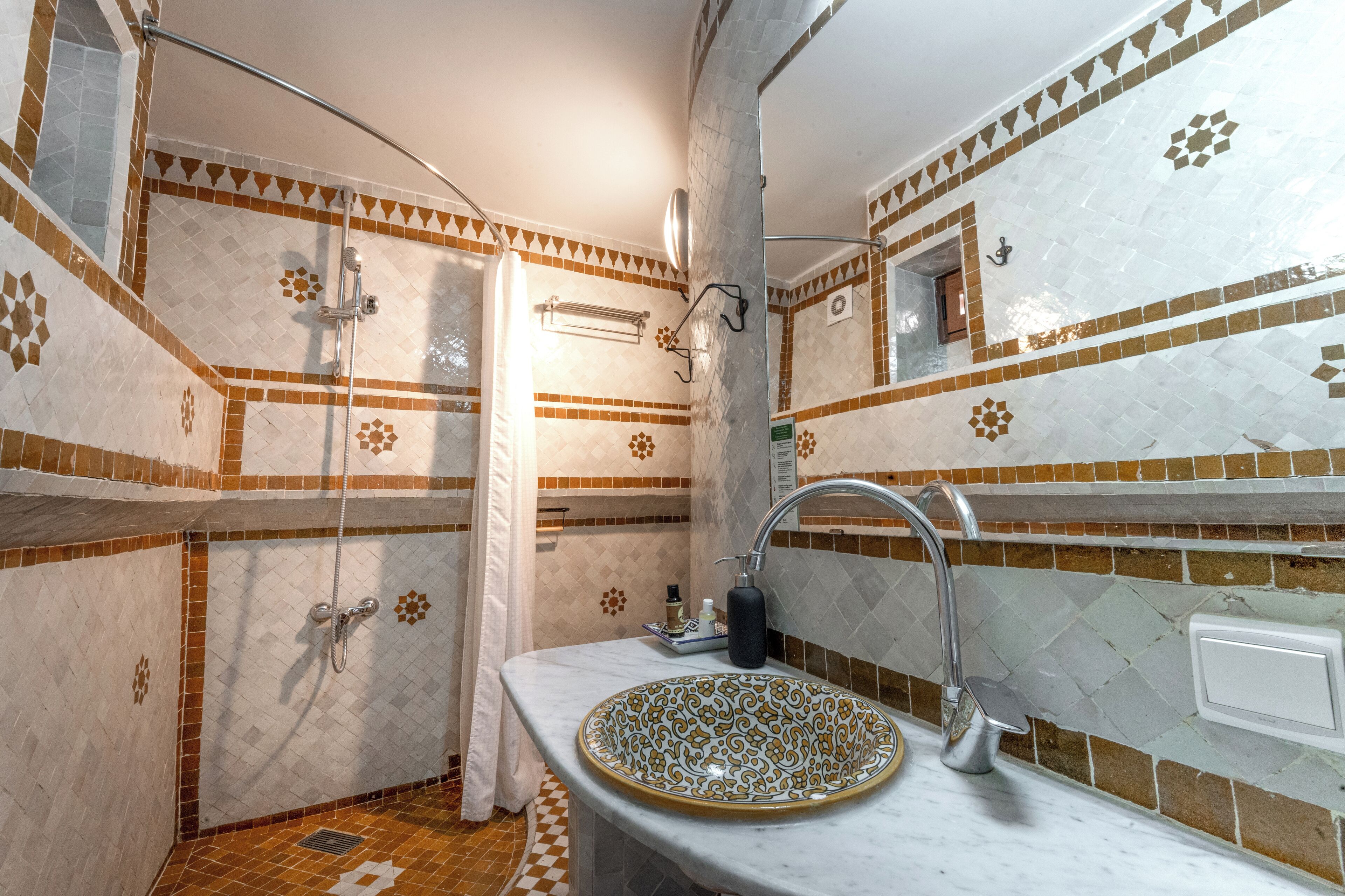 Un baño con un lavamanos grande y decorativo, ducha con puerta de cristal y paredes con azulejos estampados.