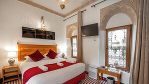 Habitación de hotel con una cama grande, televisión, ventana con vistas y una mesita con lámpara.