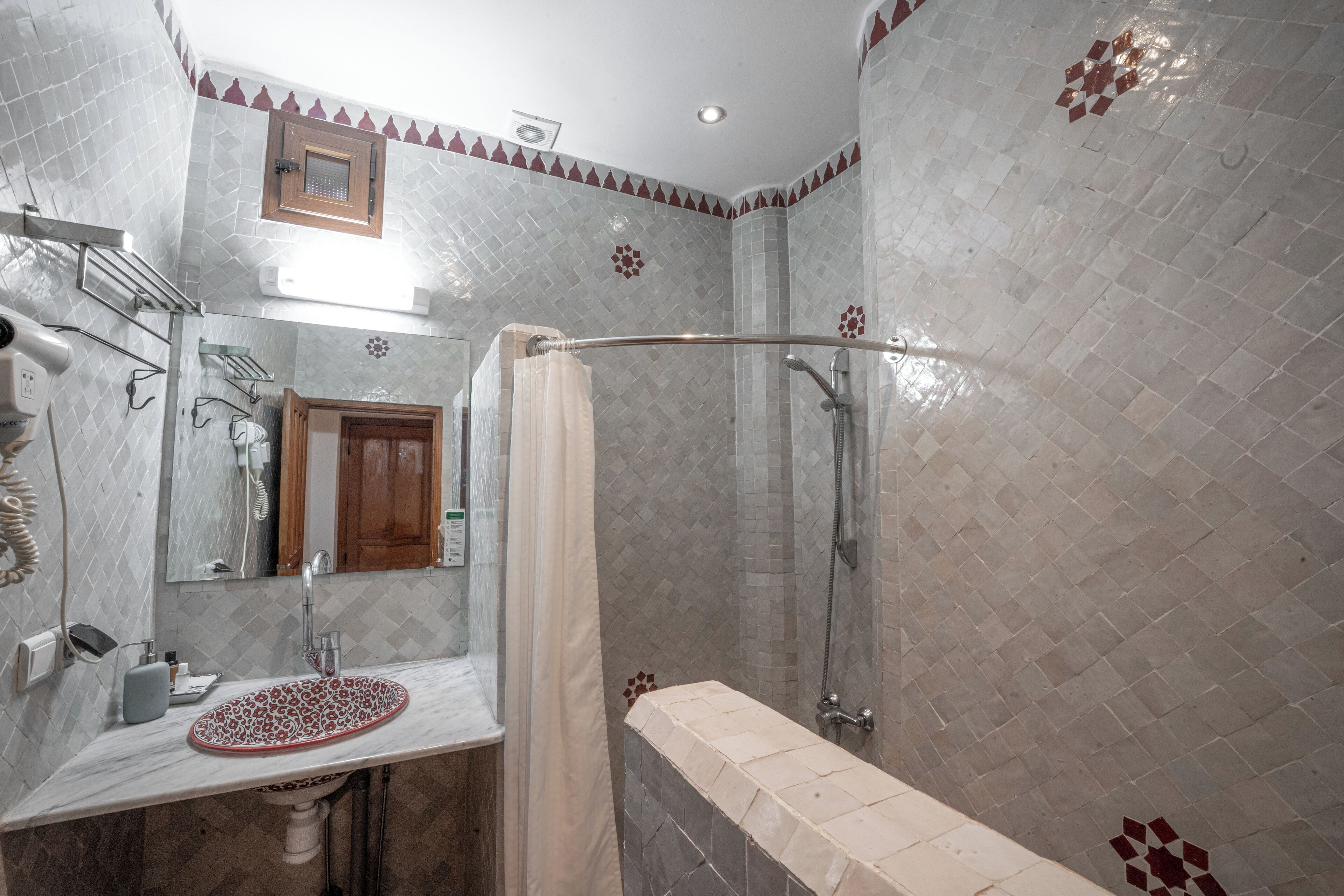 Un baño con lavamanos de mármol, cabina de ducha de vidrio y pared de ducha con azulejos.