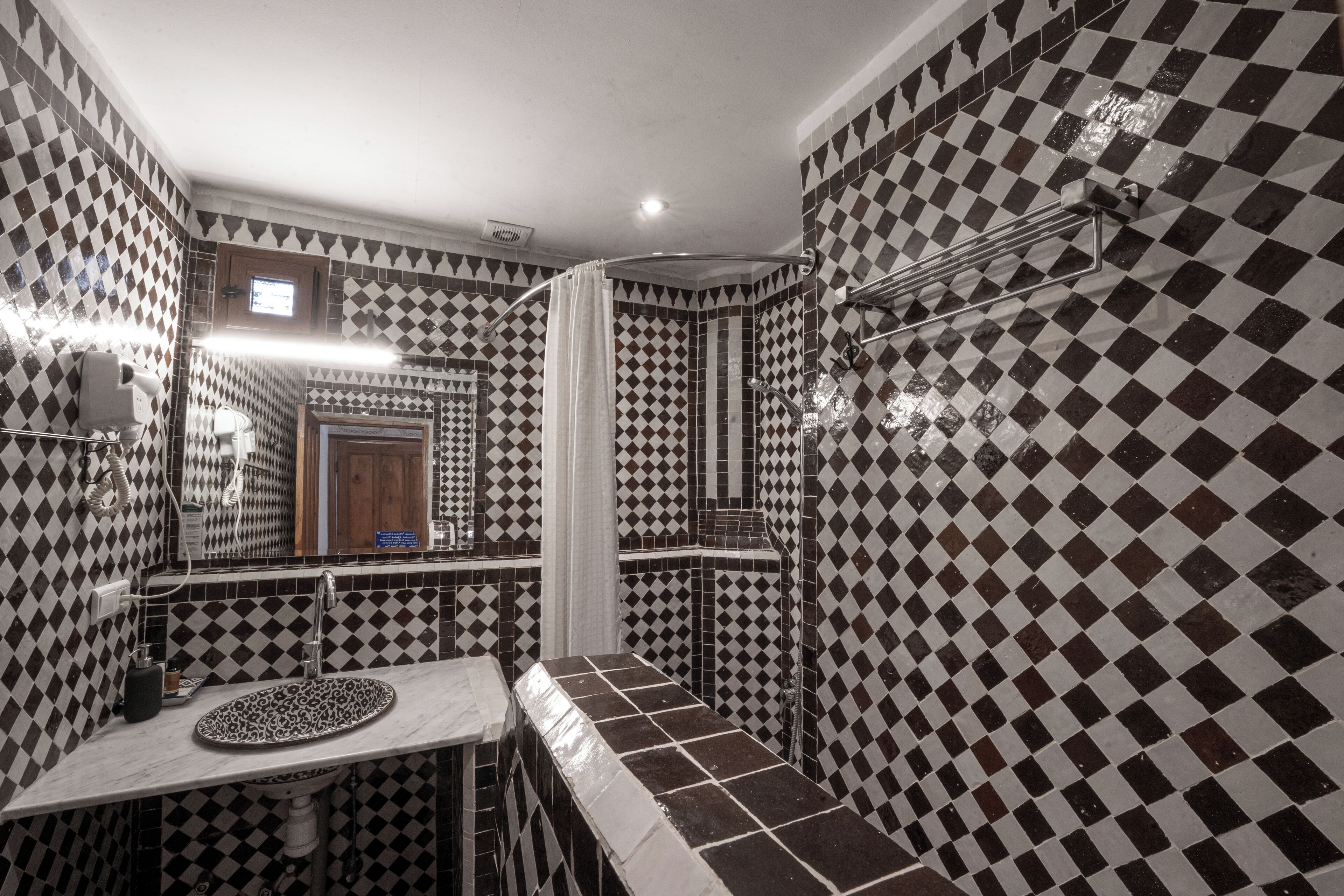 Une salle de bain avec un carrelage à motifs à carreaux, un lavabo, un miroir et un espace douche.
